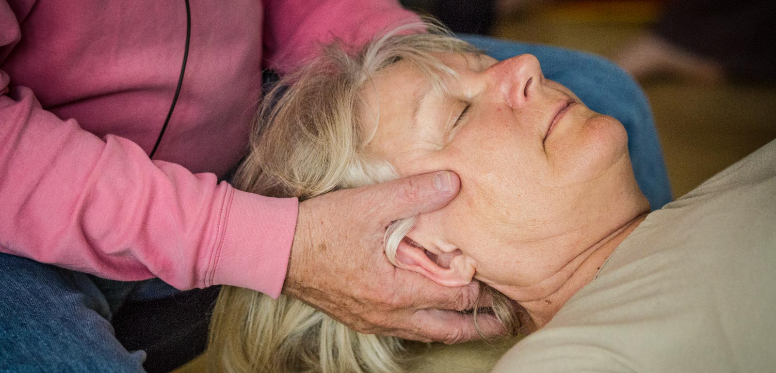 Dame bei einer Feldenkrais Einzelbehandlung. Ihr Kopf liegt in zwei Händen, sie hat die Augen geschlossen.