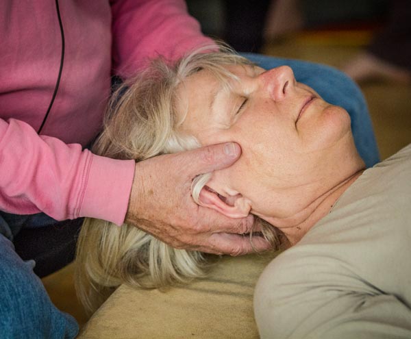 Foto von Dame bei einer Feldenkrais Einzelbehandlung. Ihr Kopf liegt in zwei Händen, sie hat die Augen geschlossen.